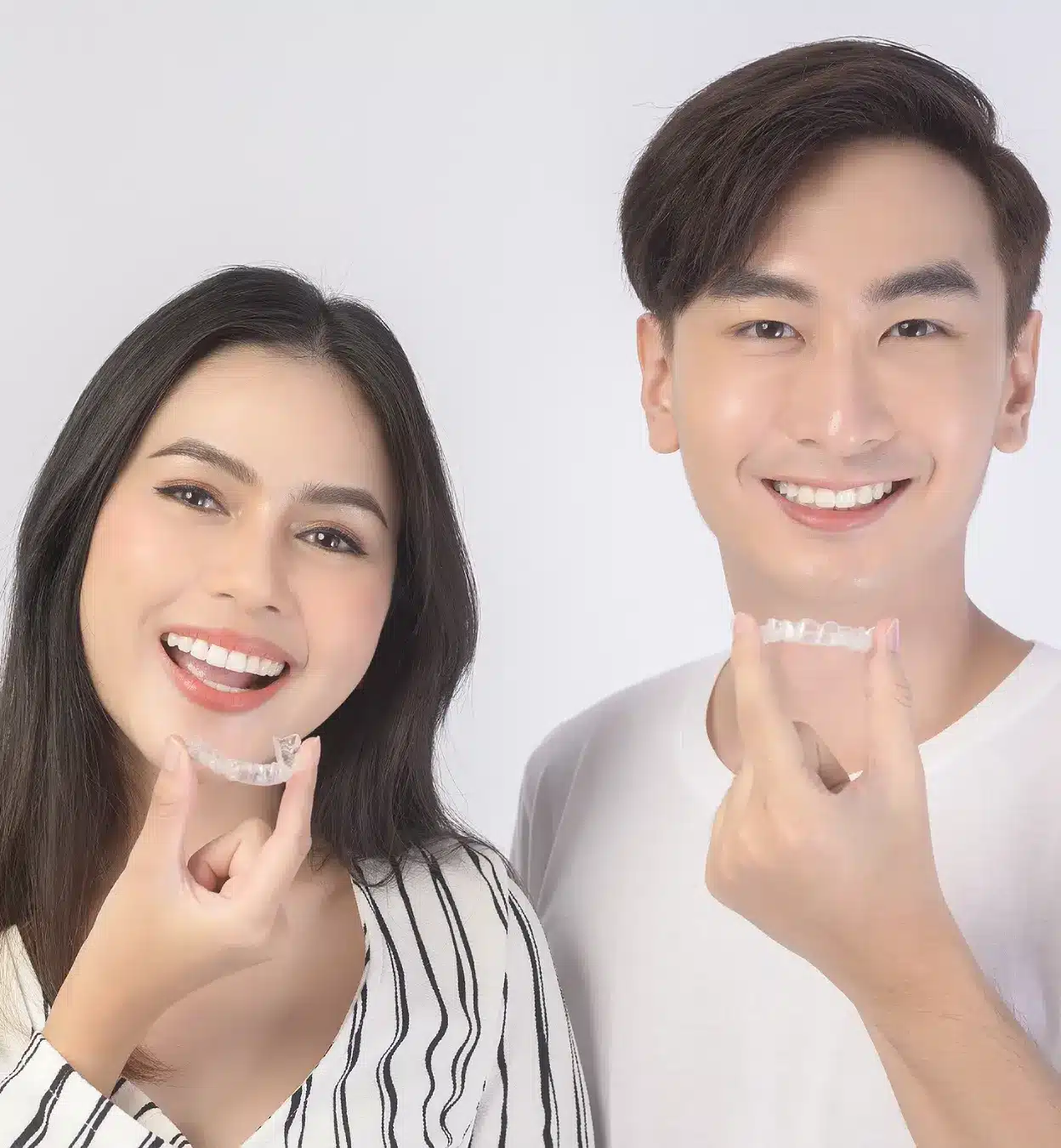 Smiling man and woman holding clear aligner trays