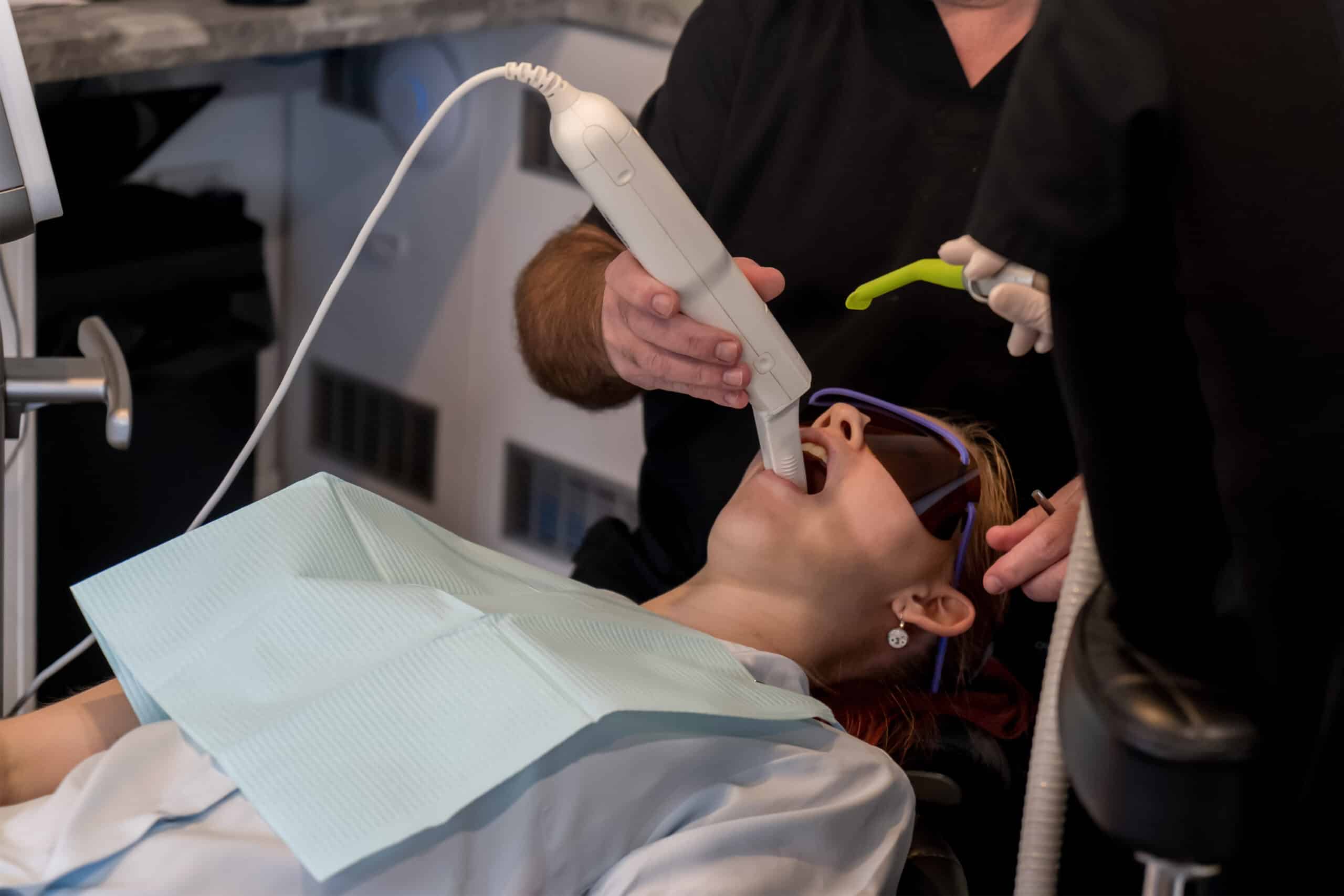 An orthodontist uses a digital handheld scanner to create a 3D dental impression for a patient.